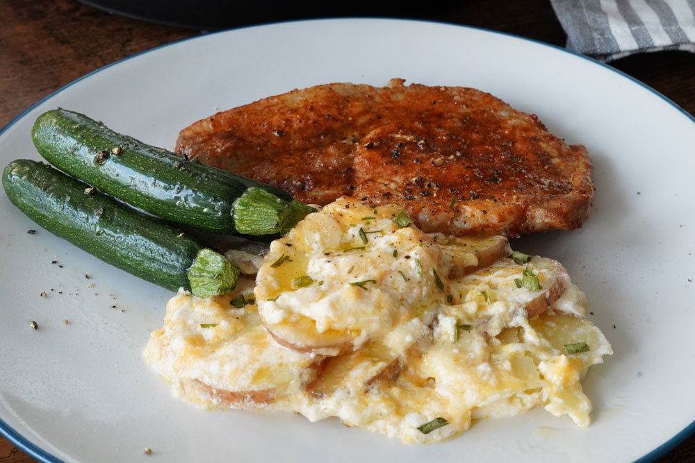 Scalloped potatoes on a plate with pork chops and zucchini